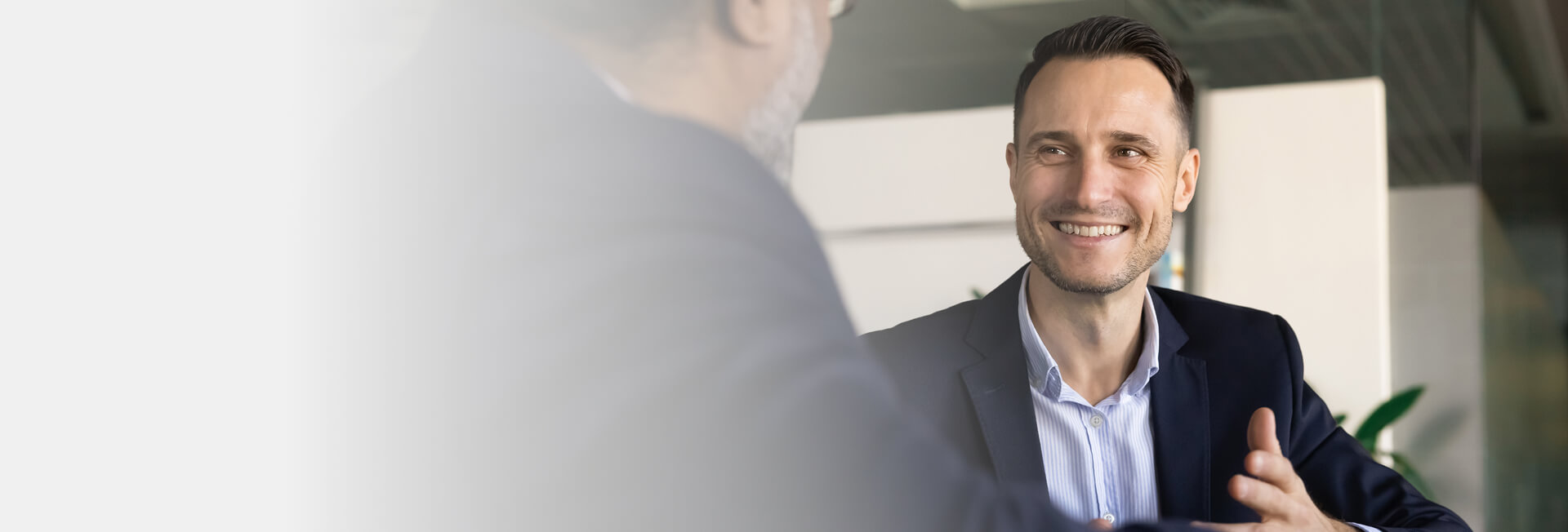 A man smiling and gesturing. He is looking at a man turned away from camera.