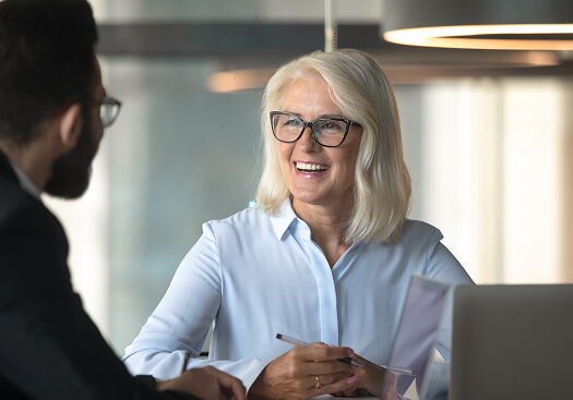 Woman smiling with another person. She sits in front of a laptop